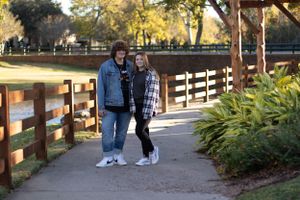 Couple in casual wear standing together on wooden bridge walkway surrounded by greenery.