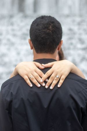 Close up of hands with rings embracing around shoulders showing engagement or wedding rings.