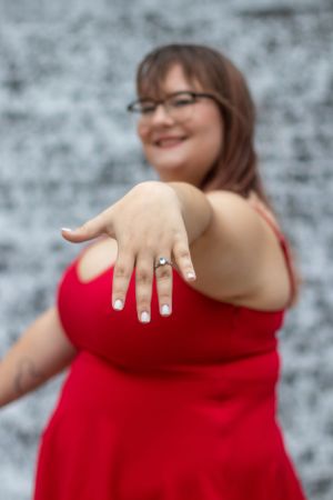 Person in red dress shows off engagement ring against textured wall.