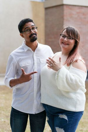 Couple in casual attire poses together while gesturing and smiling.