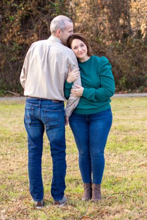 Couple embracing outdoors on grass while wearing casual clothing.