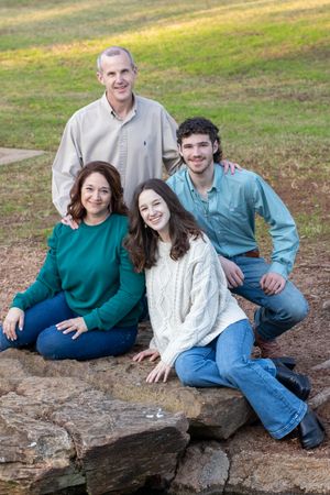 Family of four sitting together on a large rock outdoors during a casual photo session.
