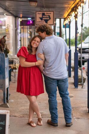 A couple shares an intimate moment under string lights outside a Texas-themed storefront.
