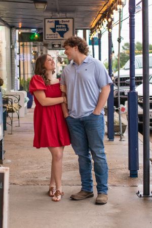 Couple sharing a romantic moment under covered walkway, wearing red dress and casual attire.