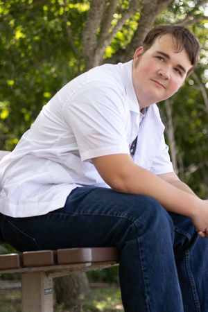 A casual portrait of someone sitting outdoors on a bench wearing a white button-down shirt and jeans.