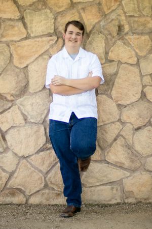 Student in white shirt and jeans poses against stone wall backdrop.