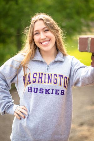 Student wearing gray Washington Huskies sweatshirt poses outdoors on campus.