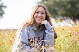 Person wearing gray sweatshirt poses outdoors among wildflowers.