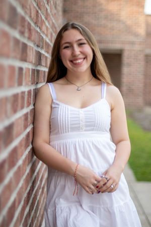 Portrait against brick wall wearing white summer dress and delicate necklace.