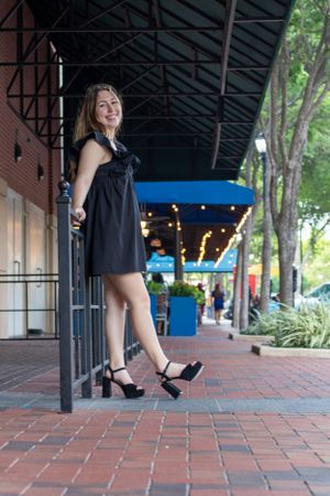 Stylish black dress and heels pose under covered walkway with string lights.