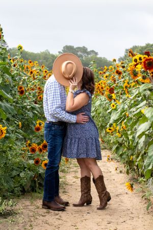 Intimate moment between couple in sunflower field with person wearing brown cowboy hat.