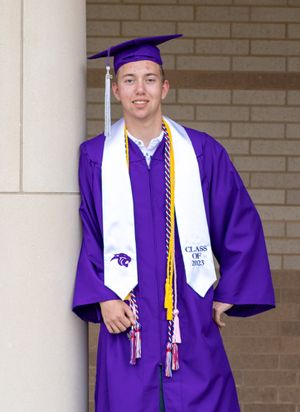 Graduate wearing purple and white graduation regalia with honor cords poses outside building.