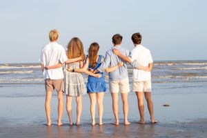 Group of five people standing together looking at ocean during beach sunset.
