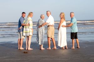 A group of people stand together on a beach at sunset wearing light summer clothing.