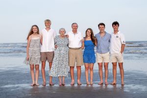 Extended family poses together barefoot on beach at sunset.