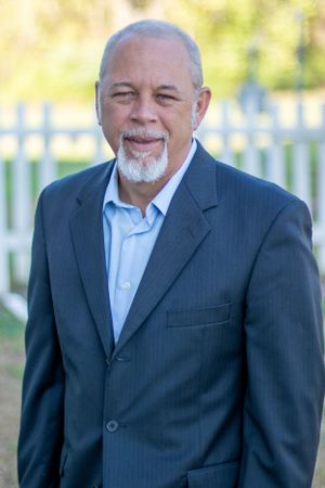 Professional headshot of a distinguished gentleman in a business suit with a white beard.