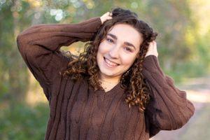 Casual outdoor portrait featuring a brown sweater and curly hair against a bokeh background.