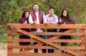 Family portrait at a wooden fence showing four people in coordinated fall colors.