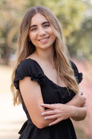 A portrait of a woman in a black ruffled dress against a blurred nature background.
