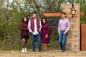 Family group photo at a rustic stone entrance wearing coordinated burgundy and pink outfits.