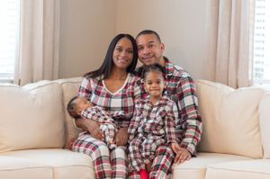 A family wearing matching plaid pajamas sits together on a beige couch.