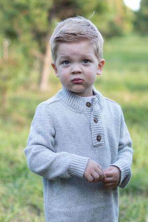 Portrait in gray knit sweater with buttons against natural outdoor background.