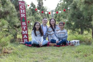 Family wearing coordinated outfits poses by Christmas sign with festive decorations.