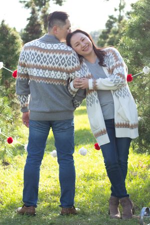 Couple wearing matching winter sweaters shares intimate moment among holiday decorations.