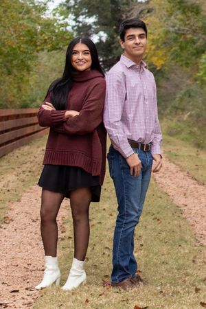 Two people pose on a nature trail wearing coordinated fall sweaters and casual attire.