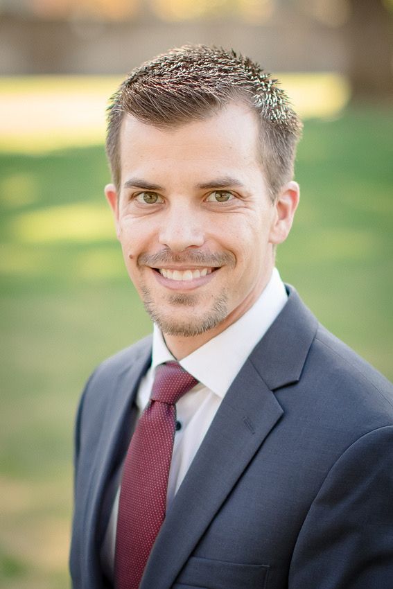 Professional portrait of person in dark suit and burgundy tie with natural outdoor lighting.