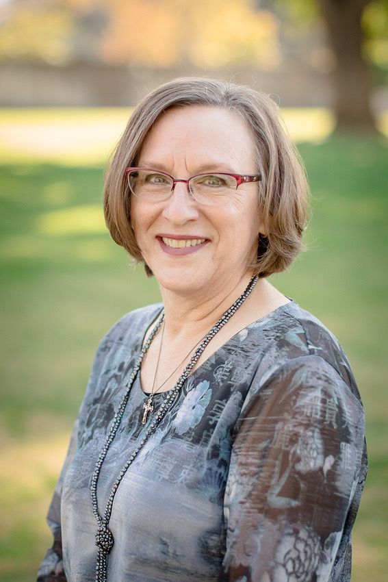 Professional portrait of person wearing gray patterned top with black beaded necklace.