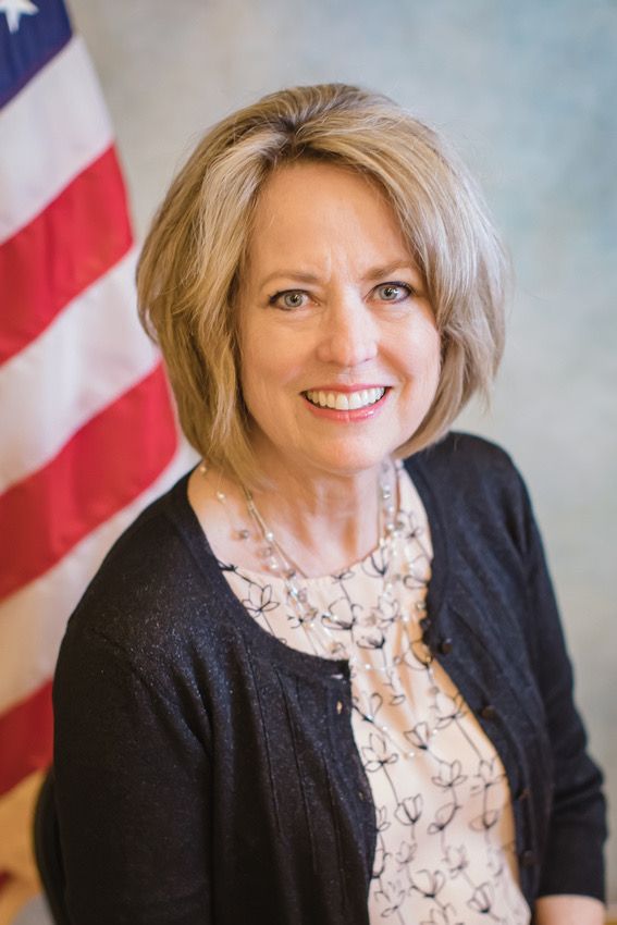 Professional portrait against American flag background wearing black cardigan and printed blouse.