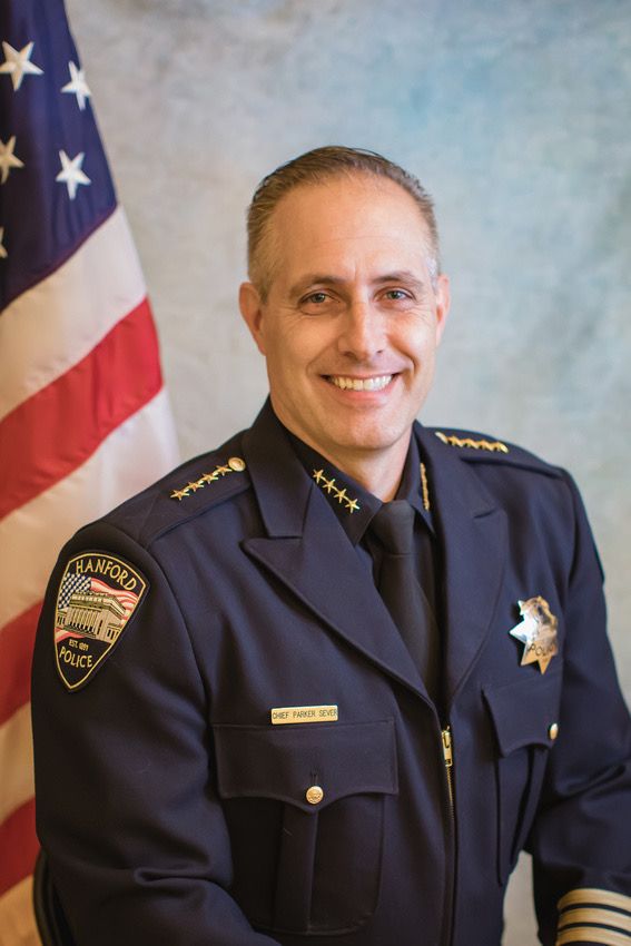 Police chief in dark uniform standing in front of American flag for official portrait.