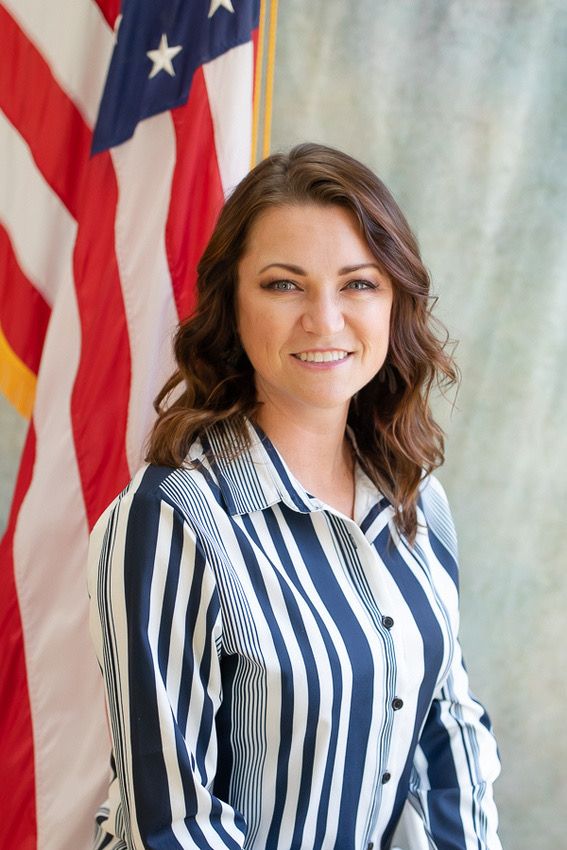 Professional portrait of person in striped blouse against American flag backdrop.