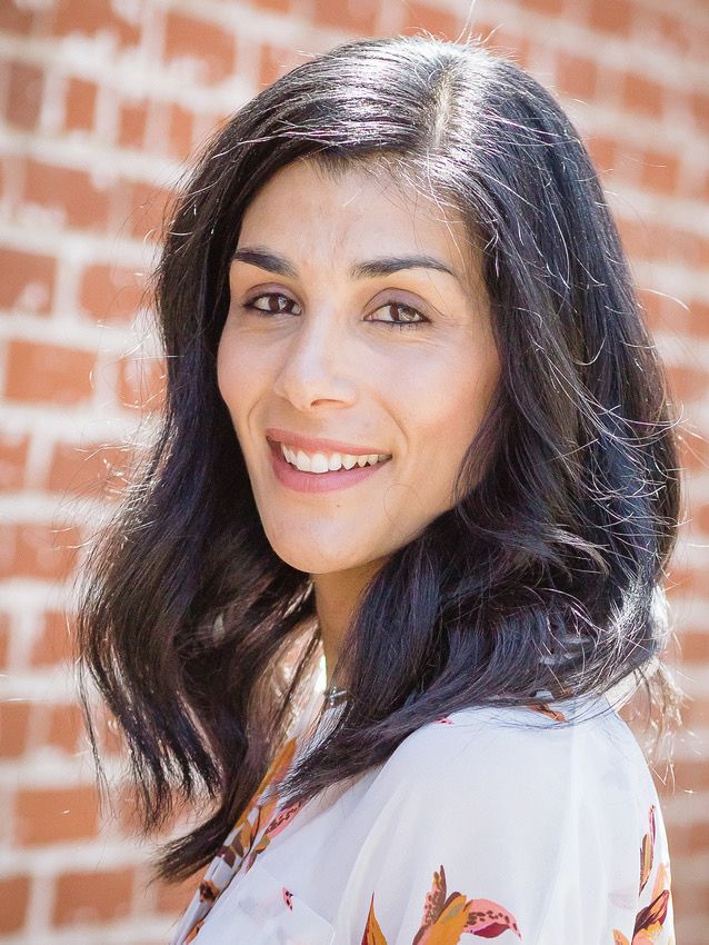 Professional headshot against brick wall background wearing white patterned top.