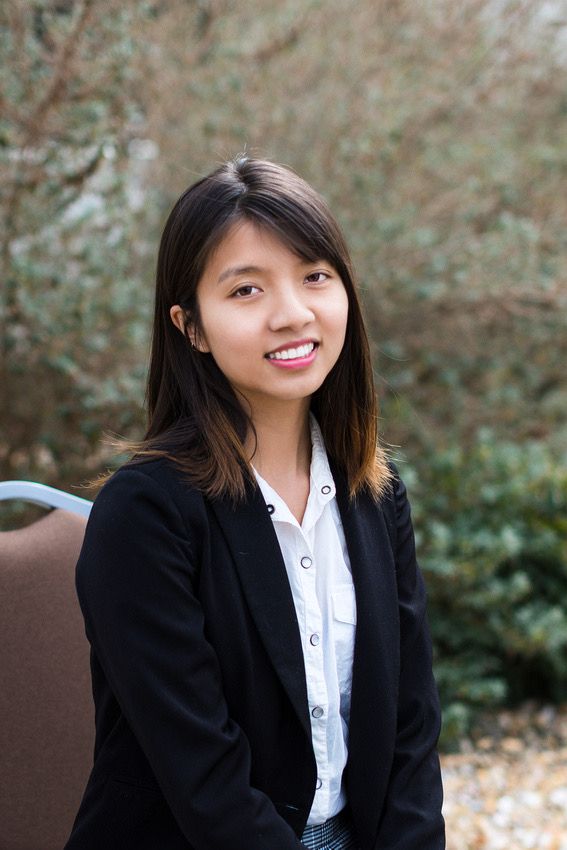 Professional portrait of person in business attire against natural outdoor background.