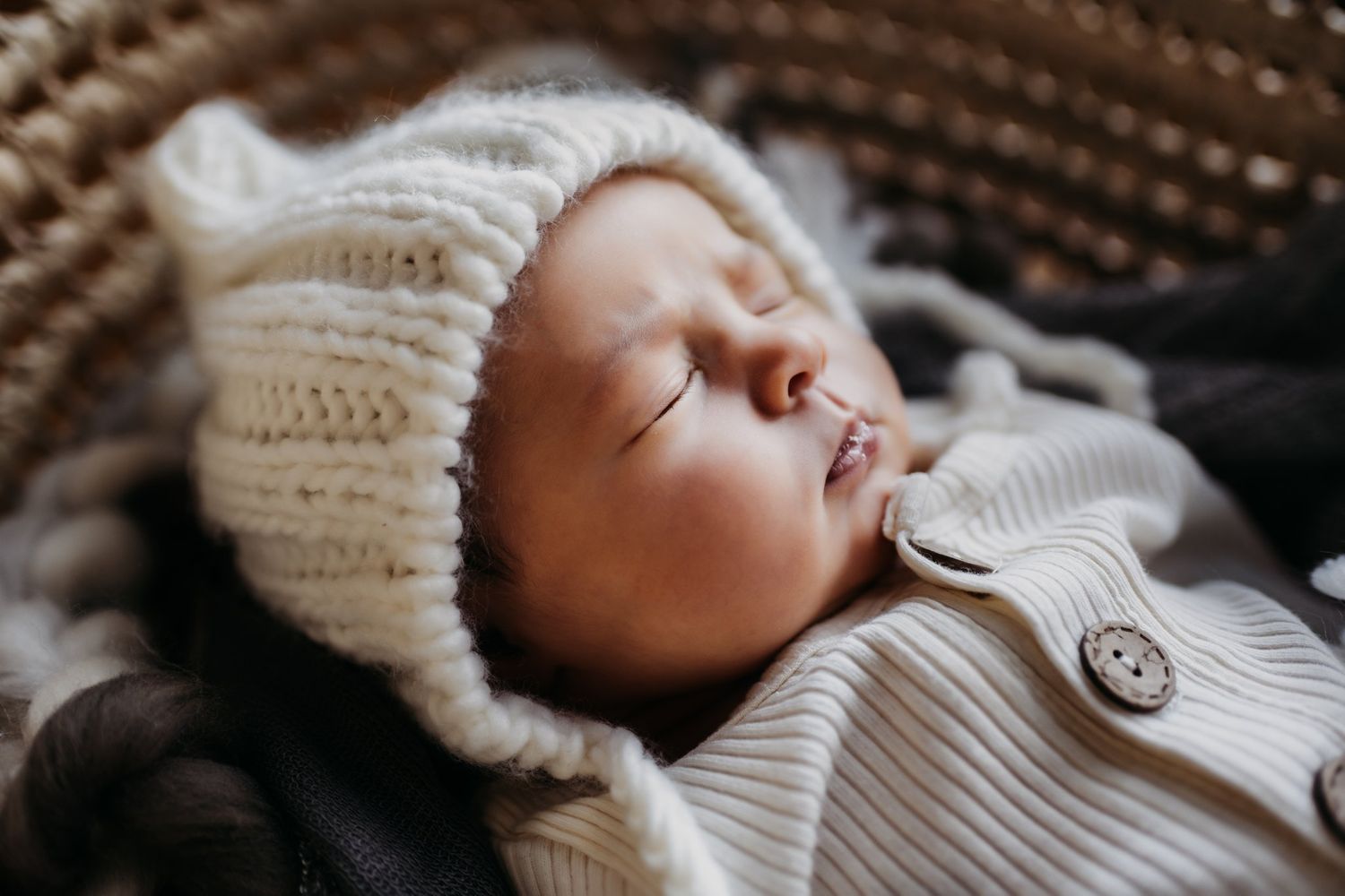 Sleeping baby wearing knit white bonnet against dark textured background.