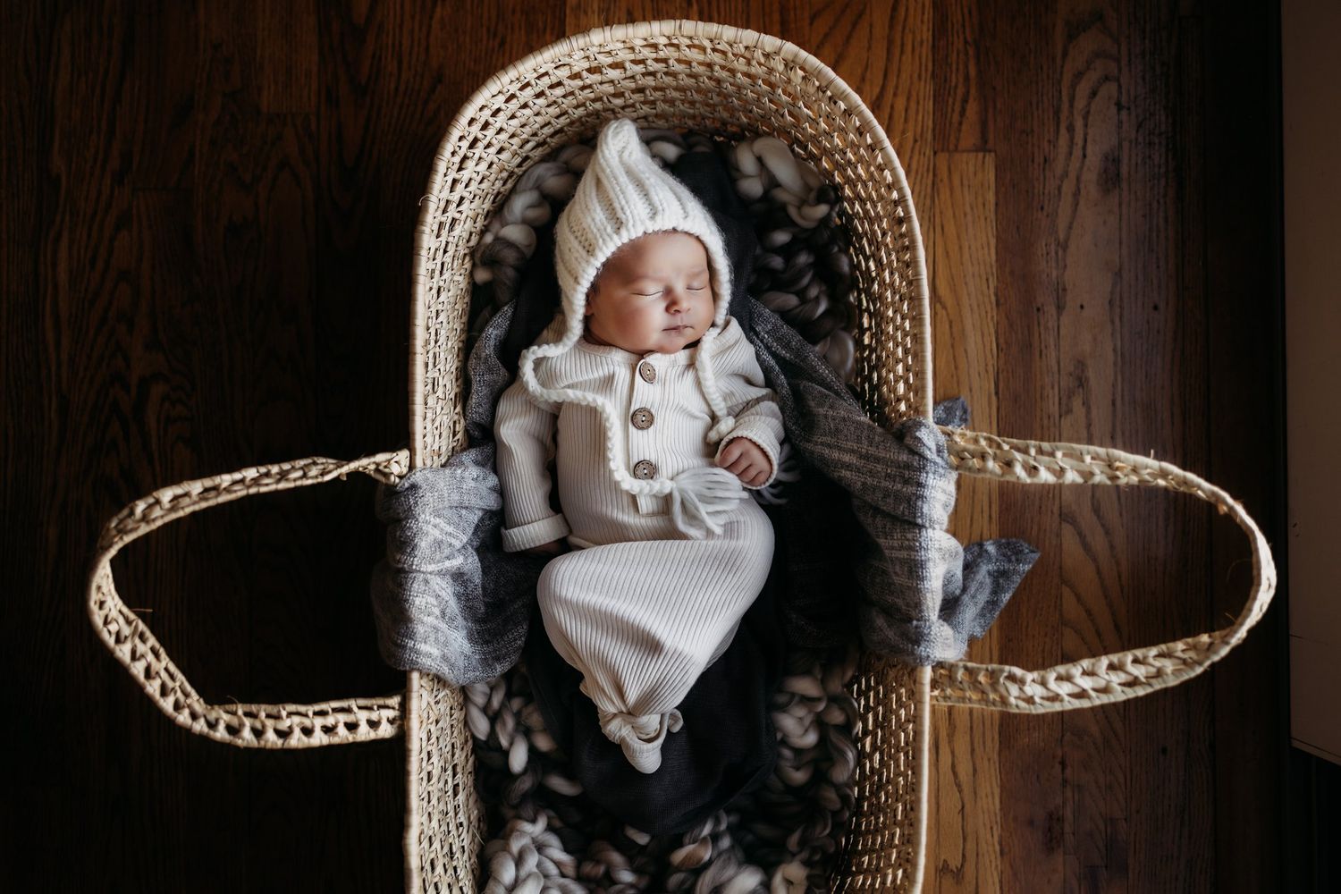Newborn in white knitwear resting in a woven moses basket lined with soft fabric.