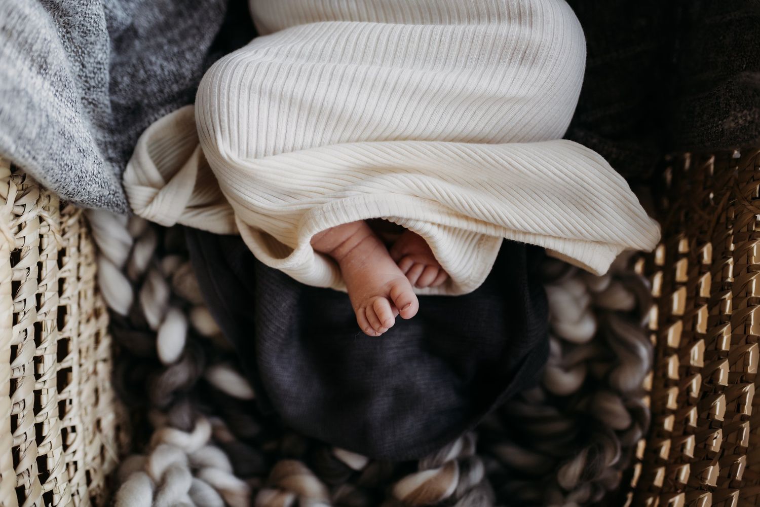 Small bare feet peeking out from white knitted clothing in woven basket.