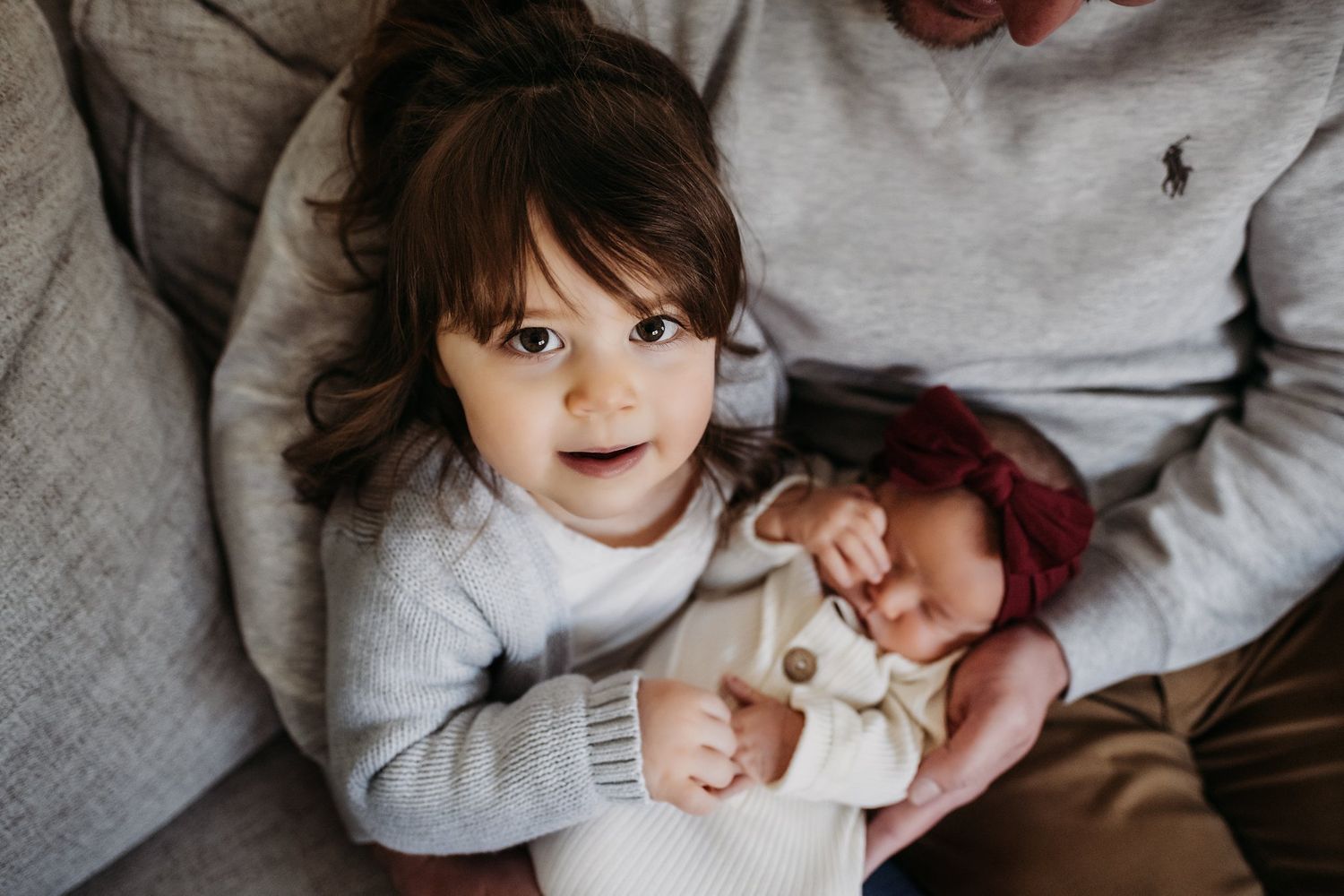 Cozy family scene with grey sweaters and warm expressions on sofa.