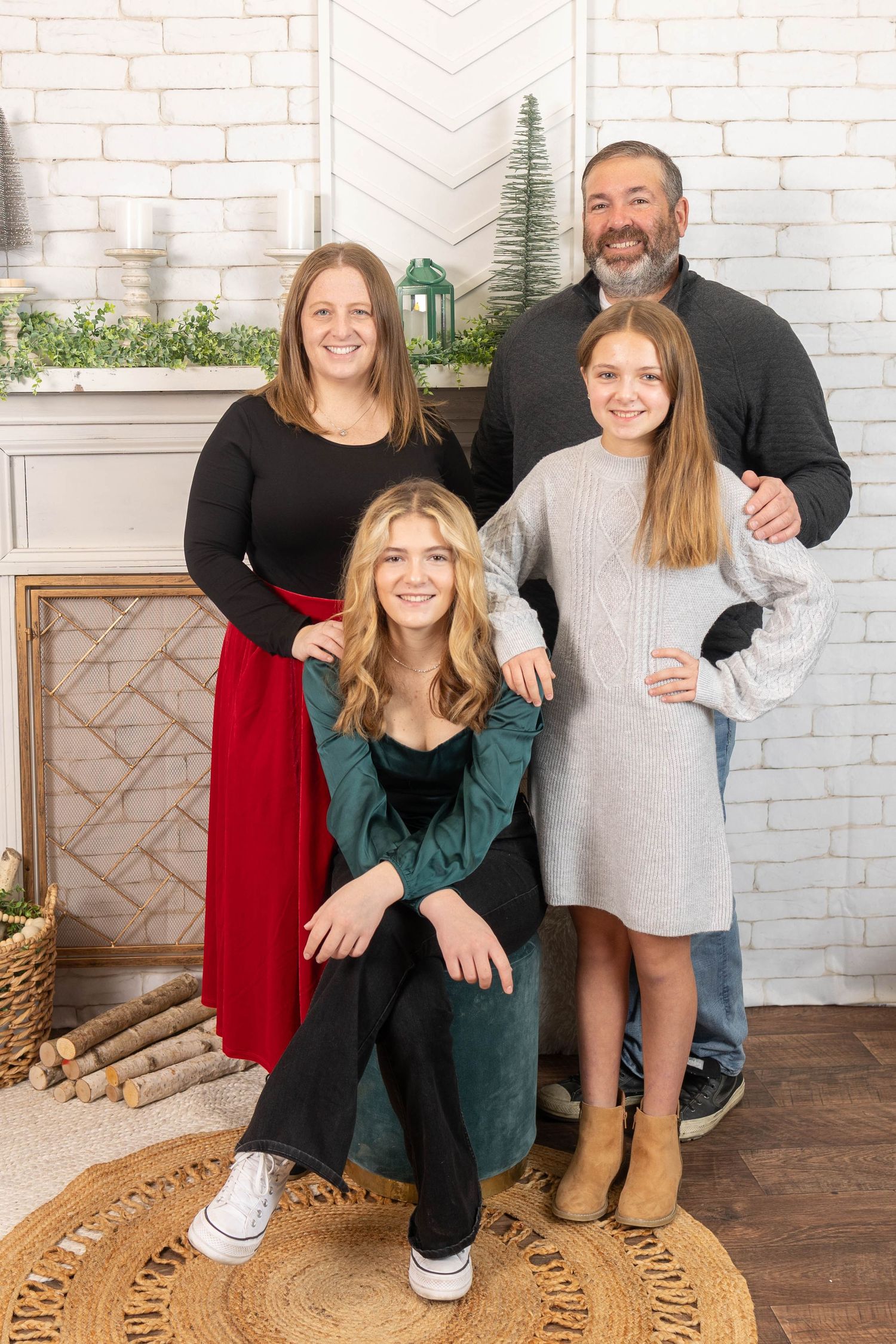 A cozy indoor family portrait against a white brick wall with holiday decorations.