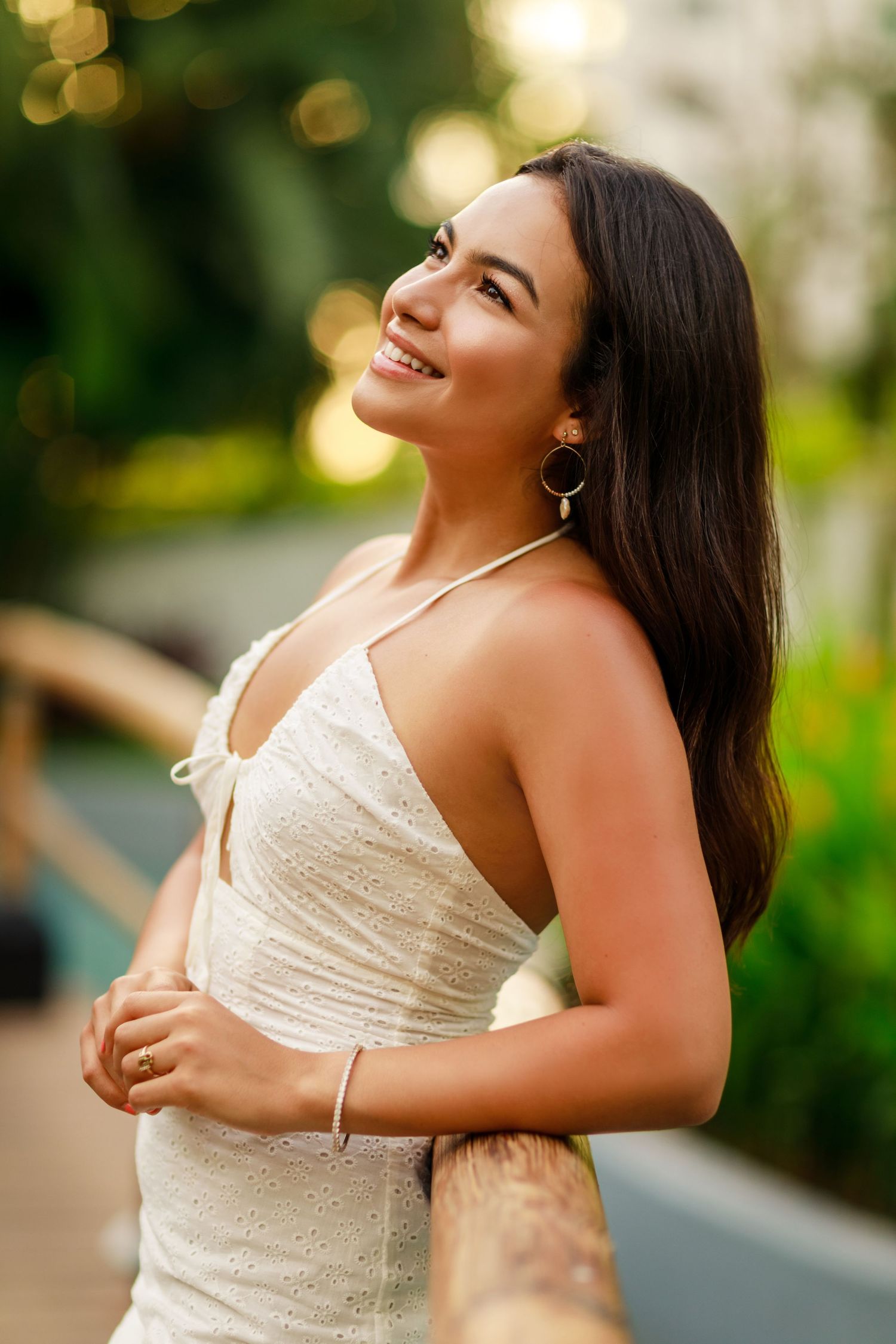 Woman in a white dress smiling outdoors with bokeh lights in the background.