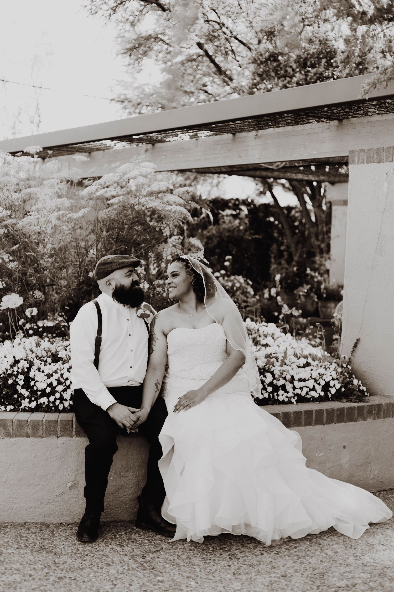 Black and white portrait of newlyweds sitting together under garden pergola.