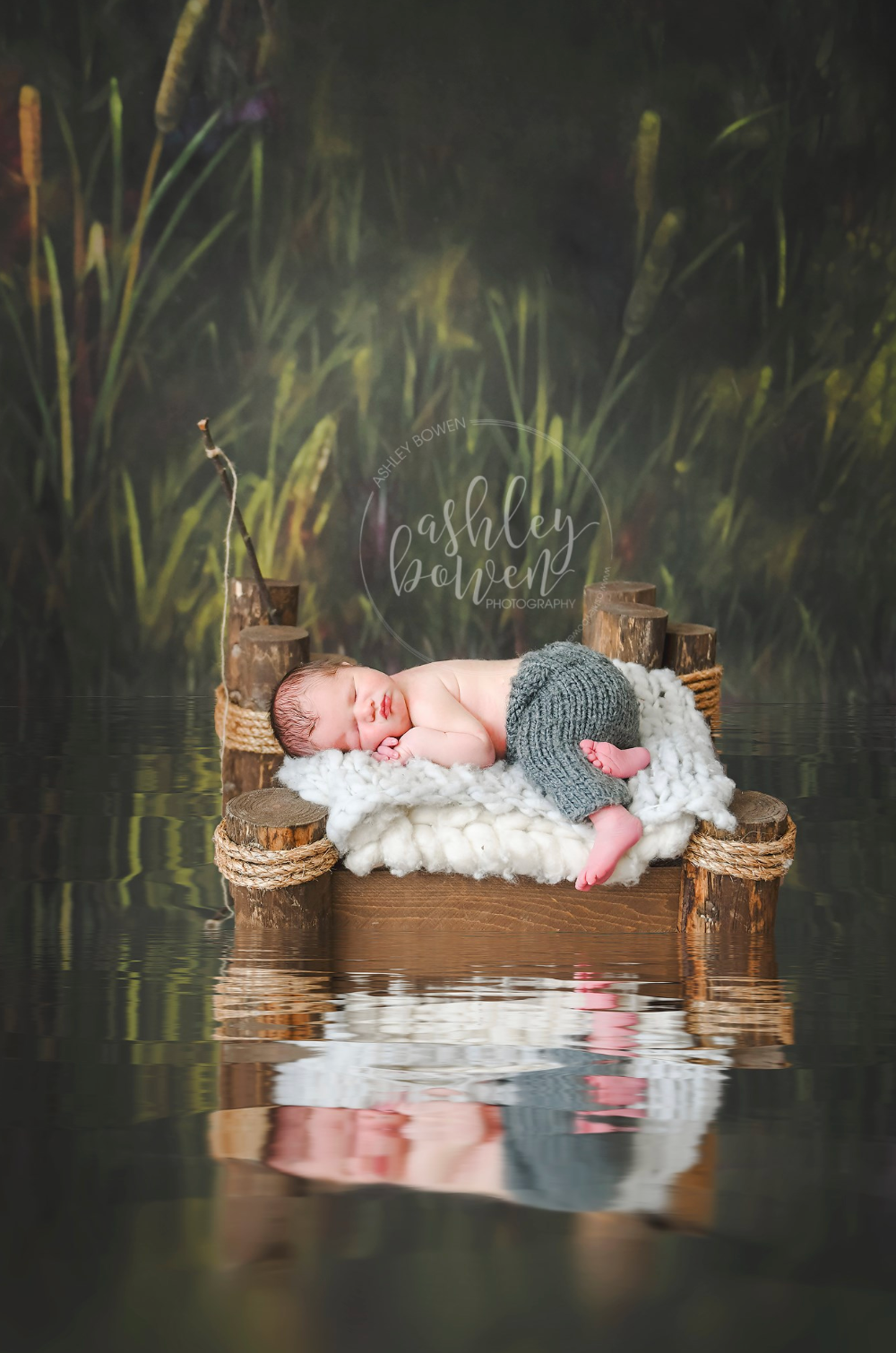 Sleeping newborn baby on rustic wooden dock surrounded by serene pond and greenery.