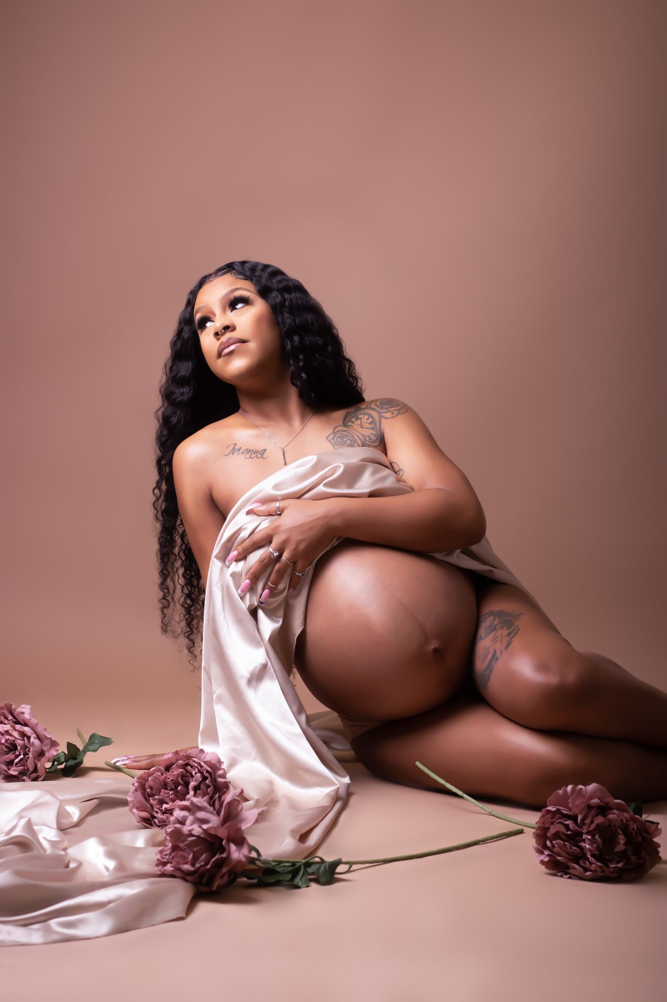 Artistic maternity photo with silk fabric and pink flowers on mauve background.