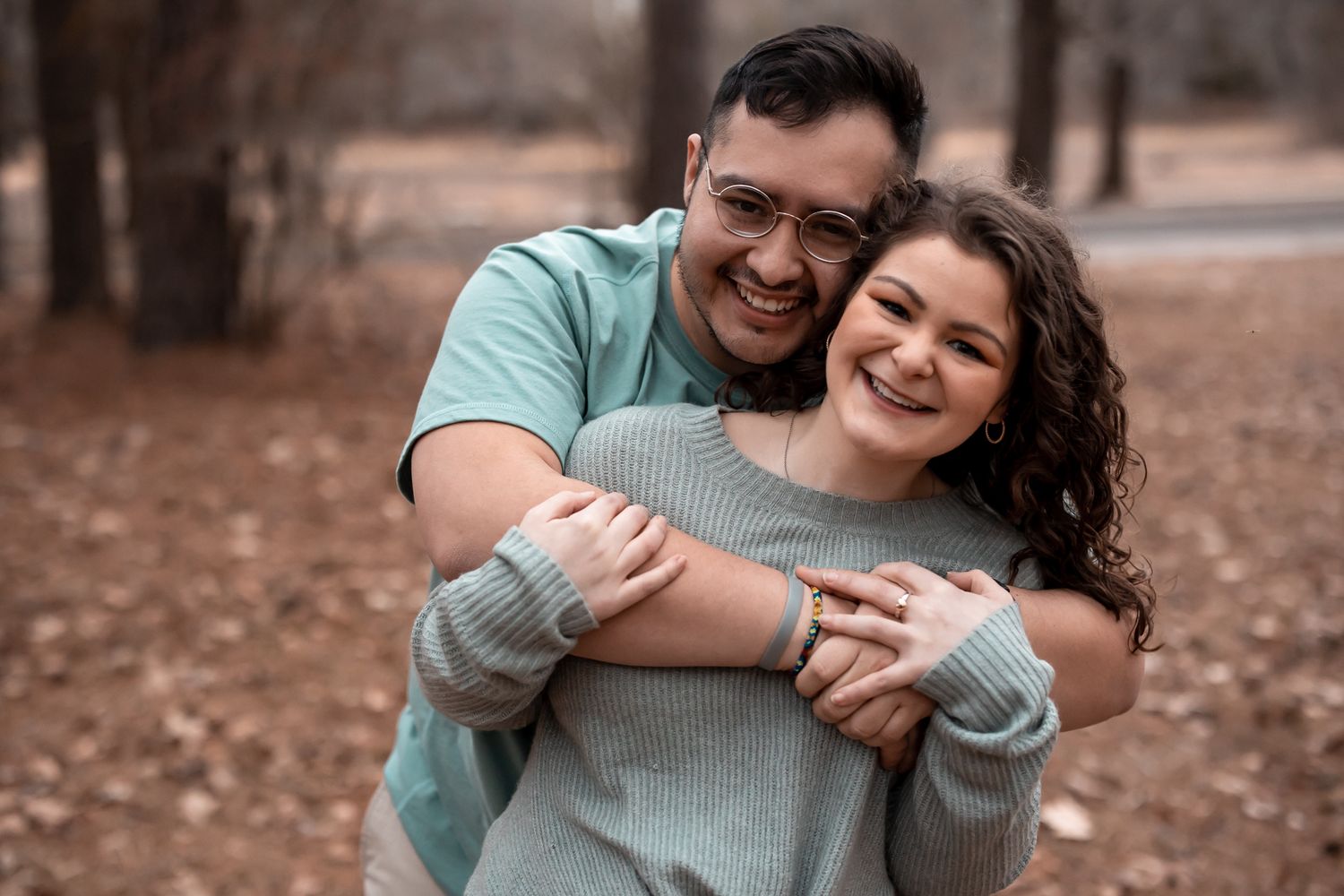 A couple shares joyful laughter while embracing outdoors in a casual autumn setting.