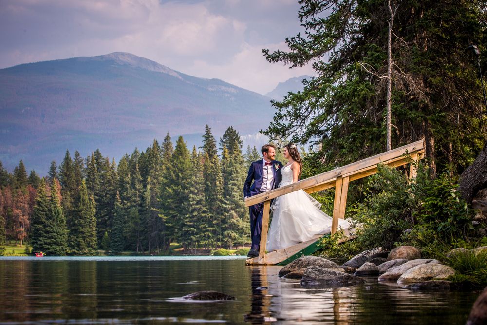 Mountain lake wedding portraits with evergreen forest and dramatic peaks in background.