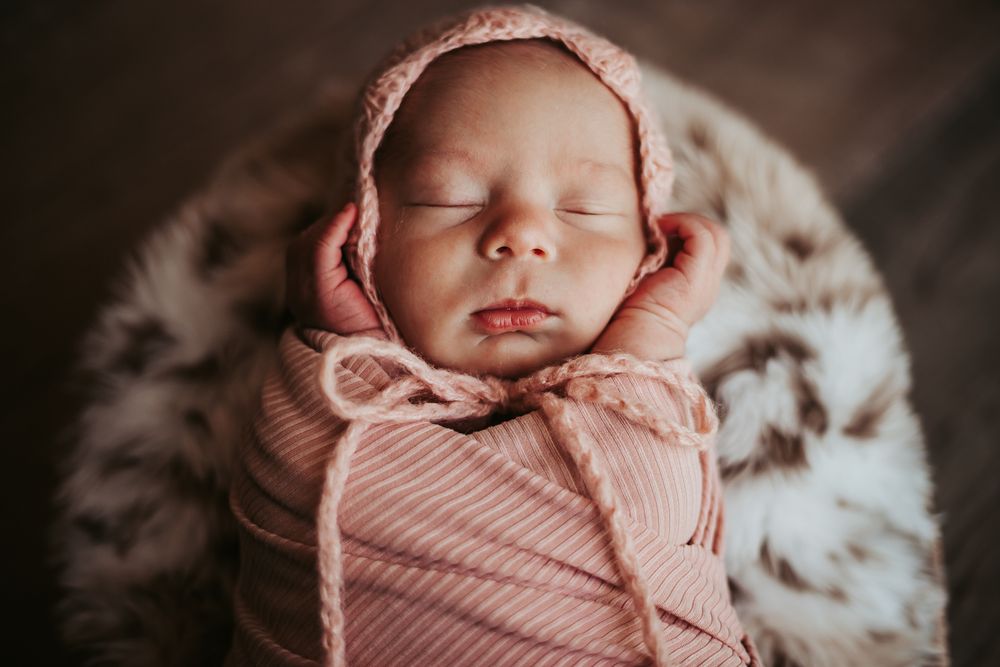 Sleeping newborn wrapped in pink swaddle against soft textured background.