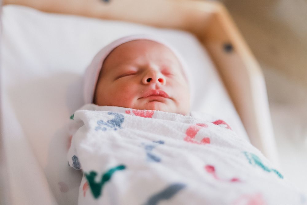 Peaceful sleeping newborn baby wrapped in floral swaddle blanket.