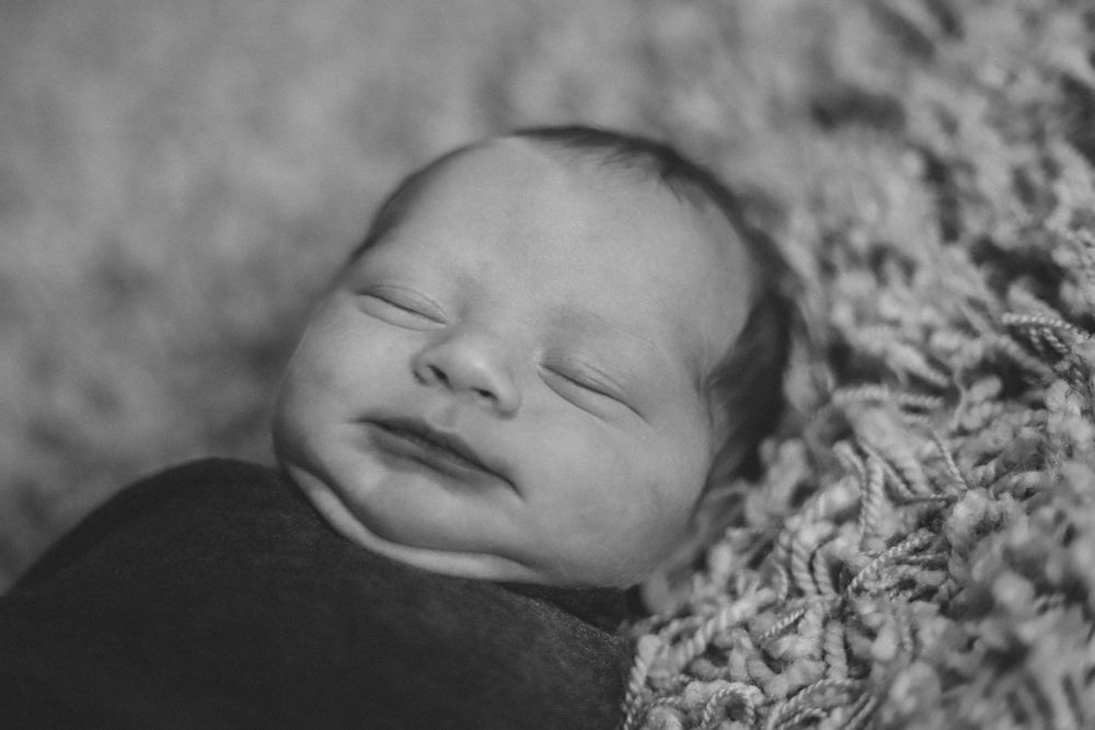Black and white close-up portrait of a sleeping newborn baby nestled in soft textured fabric.